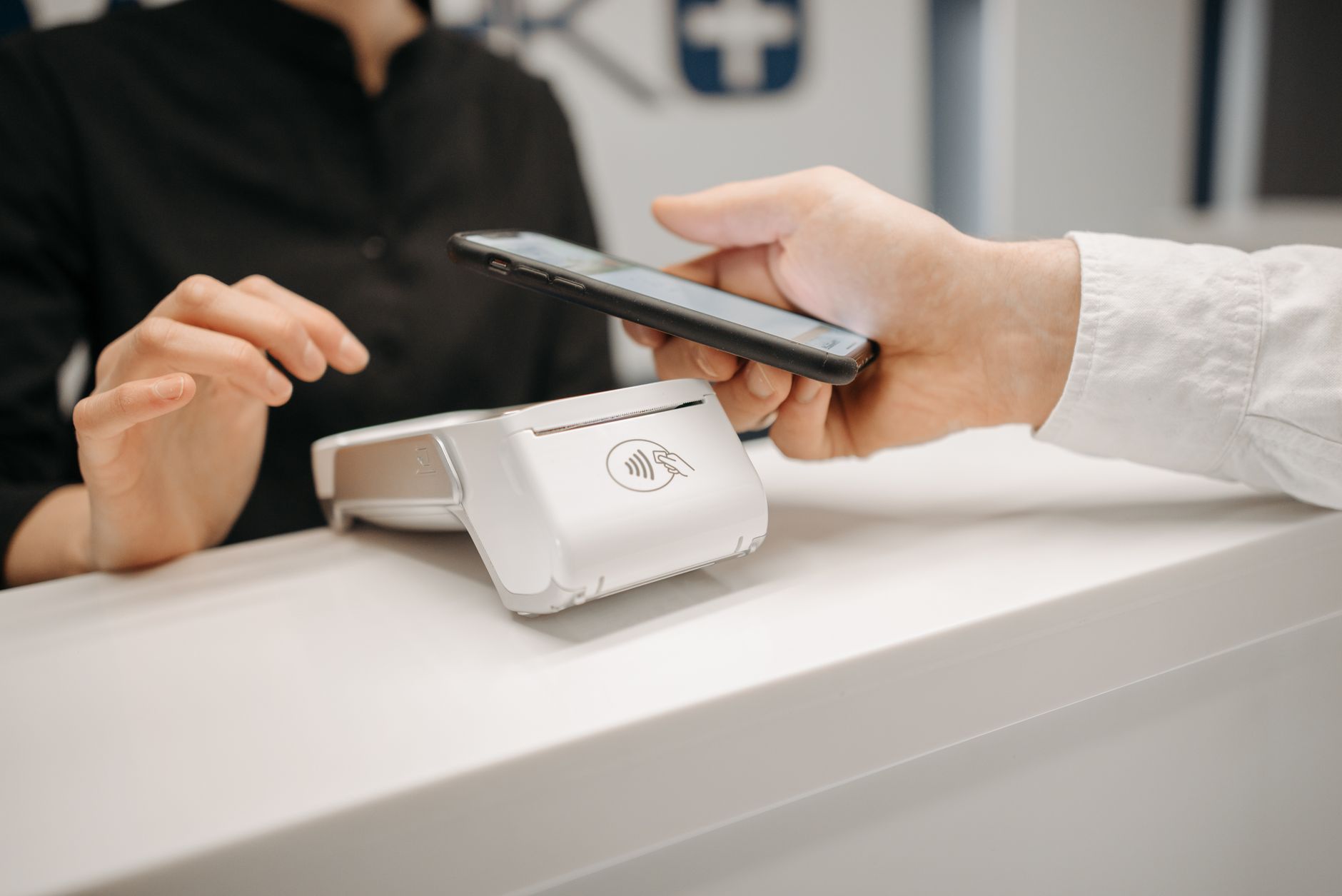 Une main tient un smartphone au-dessus d’un terminal blanc posé sur un comptoir.